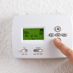 A picture of a person pressing a button on a thermostat for an energy efficient HVAC system