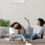 mother and daughter sitting on couch with air conditioning remote